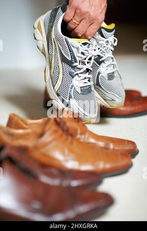 Scarpe per ogni occasione. Scatto corto di un uomo che afferra le sue scarpe da running tra le sue scarpe formali. Foto Stock