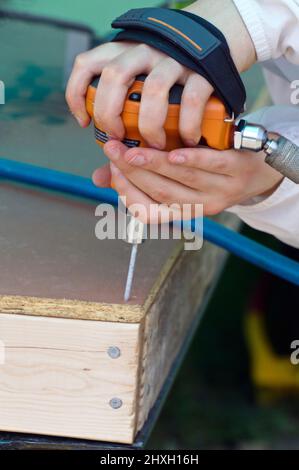 Chiudere fino a una giovane donna con le mani in mano utilizzando un palm chiodatrice utensile punzone rapidamente i chiodi in una tavola di compensato Foto Stock