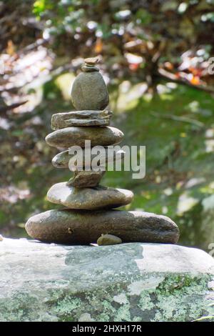 Un mucchio di pietre di fiume impilate che creano un cairn delicatamente equilibrato per marcare un sentiero escursionistico foresta in estate Foto Stock