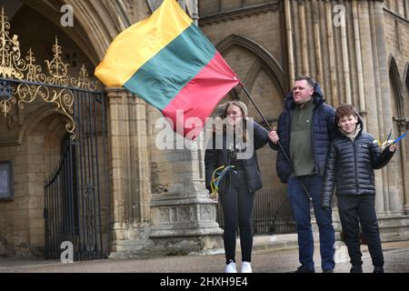 Peterborough, Regno Unito. 12th Mar 2022. Alla cerimonia di preghiera arriva un padre con una bandiera lituana con i suoi figli con bandiere lituane dipinte sulle guance. In un momento in cui l'Ucraina è sotto attacco da parte della Russia di Vladimir Putin, i lituani celebrano la Giornata dell'indipendenza per il restauro nella Cattedrale di Peterborough. Essi sostengono l'Ucraina e detengono le bandiere e i nastri ucraini. La Lituania ha riconquistato la propria libertà dall'Unione Sovietica il 11th 1990 marzo. Una breve preghiera e un minuto di silenzio sono stati tenuti per i caduti difensori della libertà. Credit: SOPA Images Limited/Alamy Live News Foto Stock