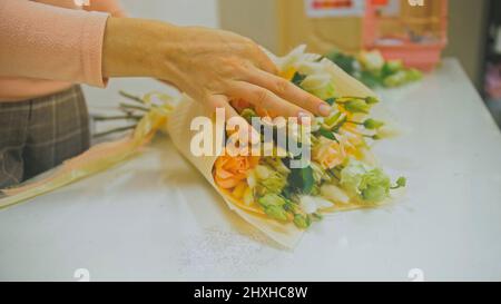 Fiorista femminile fa il mazzo di fiori, taglia fuori carta di imballaggio che lavora in negozio di fiori. Carino giovane caucasico professionale fa bouquet in vendita in Flo Foto Stock