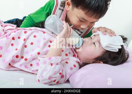 Sorella malata sdraiata e succhiare il latte sul letto, gentilmente fratello tenere veglia su un malato di vicino. Immagine concettuale sull'amore e il legame del fratello. Foto Stock