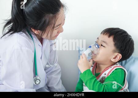 Bambino felice che ha malattia respiratoria aiutato dal professionista della salute con inalatore. Pediatra prendersi cura del ragazzo asiatico con problemi di asma rendendo l'inalazione Foto Stock