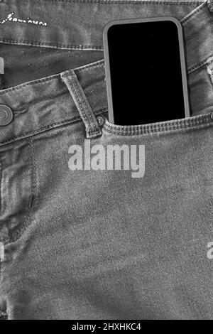 La parte superiore dei vecchi jeans neri indossati e uno smartphone con schermo nero Foto Stock