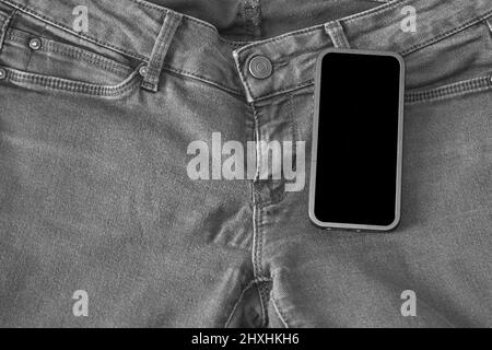 La parte superiore dei vecchi jeans neri indossati e uno smartphone con schermo nero Foto Stock