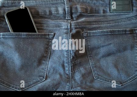 La parte superiore dei vecchi jeans neri indossati e uno smartphone con schermo nero Foto Stock