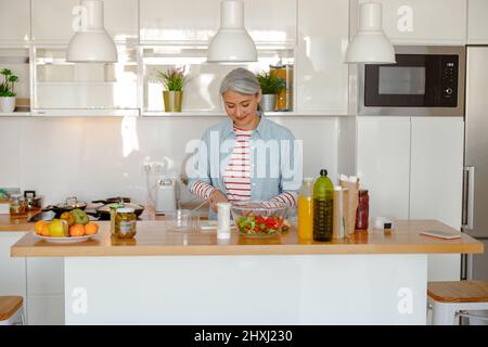 Donna sorridente che prepara insalata fresca in cucina a casa
