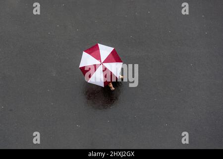 Donna con ombrello rosso e bianco per strada. Vista dall'alto. Foto Stock