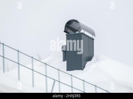 Elegante camino rettangolare in metallo sul tetto della casa. Sulla superficie c'è neve bianca. Sullo sfondo di un cielo grigio. Nuvoloso giorno d'inverno, luce tenue. Foto Stock