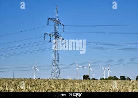 Pilone elettrico con linee elettriche e turbine eoliche sullo sfondo visto in tedesco Foto Stock