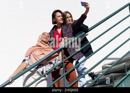 Allegre donne multirazziali che prendono selfie su smartphone su scale Foto Stock