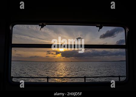 Vista dall'interno di un treno Southend Pier Railway che guarda fuori dalla finestra sopra l'estuario del Tamigi al tramonto con sole basso Foto Stock