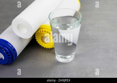 Un bicchiere di acqua pulita accanto al filtro di purificazione dell'acqua. Il concetto di sistema di filtrazione domestico. Foto Stock