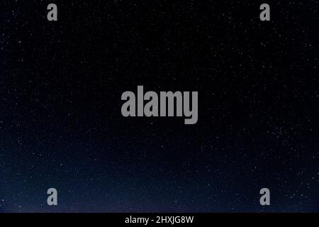 Notte, nero, cielo nuvoloso coperto da stelle incandescenti. In lontananza, sulla linea dell'orizzonte, potete vedere il bagliore e le luci di una città vicina. Foto Stock