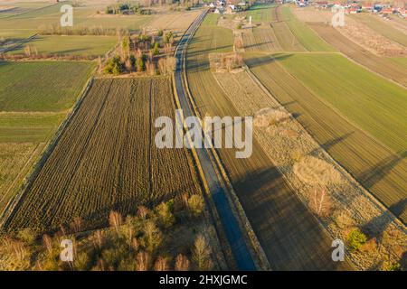 Una vasta pianura, campi arabili e prati tra i quali si può vedere una strada asfaltata grigia. È una giornata di sole, le auto sono alla guida su strada. Foto dal drone Foto Stock