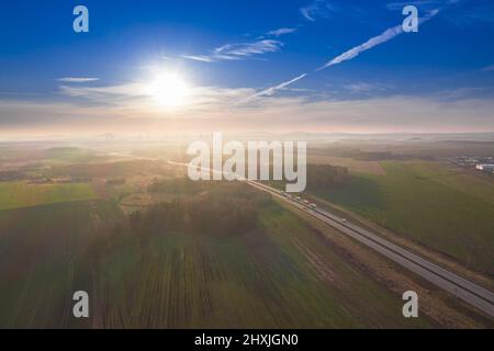 Una vasta pianura, campi arabili e prati tra i quali si può vedere una strada asfaltata grigia. È una giornata di sole, le auto sono alla guida su strada. Foto dal drone Foto Stock