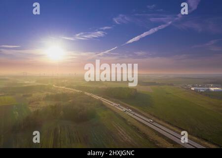 Una vasta pianura, campi arabili e prati tra i quali si può vedere una strada asfaltata grigia. È una giornata di sole, le auto sono alla guida su strada. Foto dal drone Foto Stock