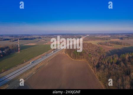 Una vasta pianura, campi arabili e prati tra i quali si può vedere una strada asfaltata grigia. È una giornata di sole, le auto sono alla guida su strada. Foto dal drone Foto Stock