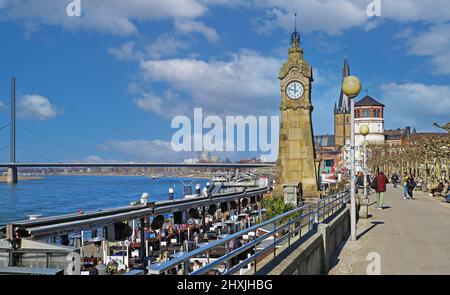 Düsseldorf (Rheinpromenade), Germania - Marzo 9. 2022: Vista sul lungofiume del reno con caffè ristoranti sulla torre dell'orologio contro il cielo blu Foto Stock