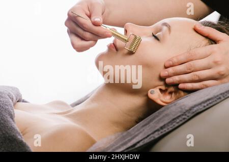 Roller gua sha massaggio di una donna in un salone di bellezza su sfondo bianco. Foto Stock