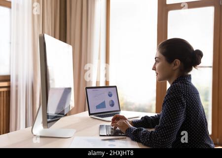 La donna indiana si siede alla scrivania analizza i diagrammi dei grafici sul pc Foto Stock