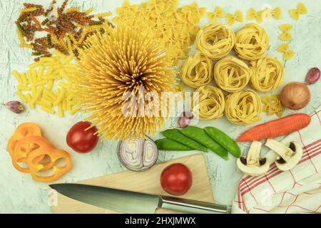 Vari tipi di pasta assortiti al tavolo. Vari tipi di pasta cruda e tagliatelle con verdure. Concetto culinario di cucina italiana. Collectio Foto Stock