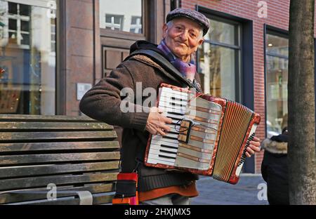 Düsseldorf, Germania - Marzo 9. 2022: Primo piano di un vecchio uomo in piedi con cappello che suona fisarmonica a piano su strade pubbliche Foto Stock