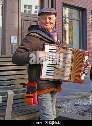 Düsseldorf, Germania - Marzo 9. 2022: Primo piano di un vecchio uomo in piedi con cappello che suona fisarmonica a piano su strade pubbliche Foto Stock