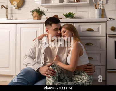 Romantica coppia sposata seduta sul piano della cucina e abbraccio. Tenero momento di famiglia. Foto di alta qualità Foto Stock