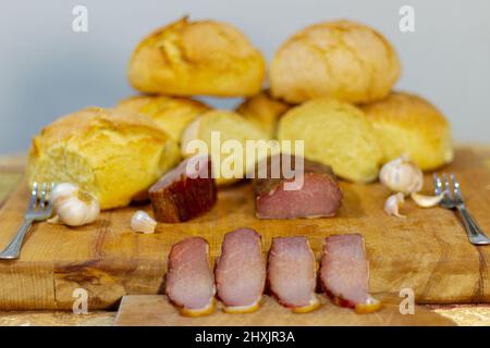 Primo piano di alimenti biologici. Affumicato di carne al tavolo con aglio e pane fatto in casa su un asse di legno. Foto Stock