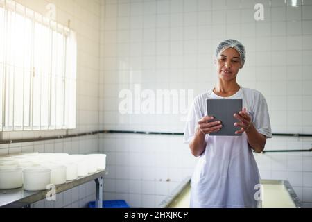 Ottenere un po 'di assistenza online. Scatto corto di una giovane lavoratrice di fattoria femminile utilizzando un tablet mentre si lavora in una fabbrica nella fattoria. Foto Stock