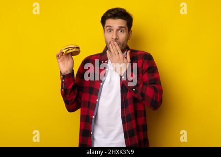 Funny Guy Holding Burger e coprire bocca Foto Stock