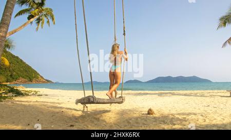 Bella donna che oscilla su un altalena su una spiaggia tropicale, sulle rive del mare turchese. Concetto di viaggio, passeggiate, riposo in mare, resort tropicale costa relax viaggio turismo vacanze estive Foto Stock