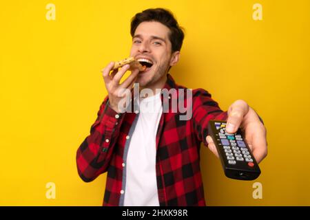Funny Guy mangiare pizza e tenere il telecomando guardare la TV Foto Stock
