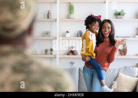 Giovane gioioso moglie Nera e bambina che accolgono il Padre militare a casa Foto Stock