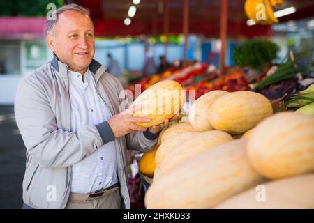 Uomo europeo di mezza età che acquista meloni freschi sul mercato della frutta. Foto Stock