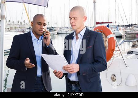 Uomini latinoamericani ed europei con documenti vicino agli yacht nel porto Foto Stock