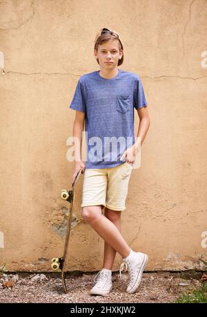 Skater dude. Sparo a tutta lunghezza di un ragazzo in piedi con il suo skateboard. Foto Stock