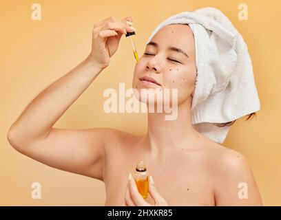 Fai cura di te stesso la tua priorità numero uno. Scatto di una giovane donna che applica un siero al suo viso durante la sua routine di bellezza mattina contro un giallo Foto Stock