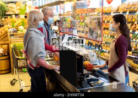 Coppia anziana in maschere facciali paganti al banco cassa al supermercato Foto Stock