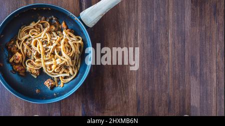 Padella in legno con spaghetti con cozze, pesce e salsa di pomodoro appena sfornata. Fatto in casa. Su tavola di legno, vista dall'alto. Orizzontale. Foto Stock