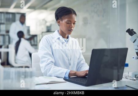 Più dura lavora, più vicina è la cura. Scatto di un giovane scienziato che usa un computer portatile mentre conduce la ricerca in un laboratorio. Foto Stock