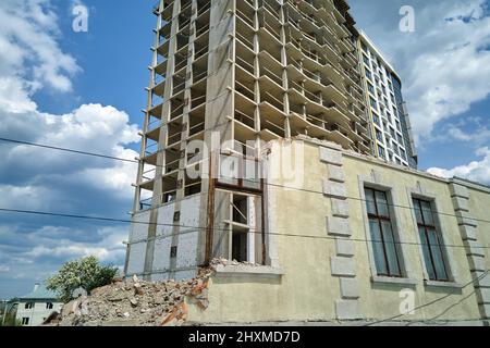 Dettaglio architettonico di alta cornice di costruzione monolitica in cemento in costruzione e vecchia casa demolita di fronte. Sviluppo immobiliare. Foto Stock