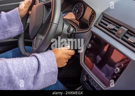 Primo piano all'interno del veicolo con la mano della donna che tiene la chiave nel commutatore di accensione e la chiave di avviamento del motore Foto Stock