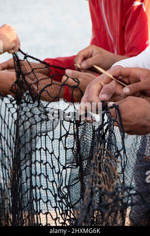 Tribunj, Croazia- 23 agosto 2021: Pescatori che riparano la rete da pesca , mano di lavoro con ago di legno dettaglio ravvicinato Foto Stock