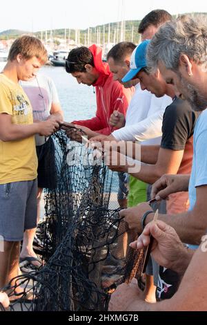 Tribunj, Croazia - 23 agosto 2021: Gruppo di pescatori che riparano la rete da pesca , primo piano Foto Stock