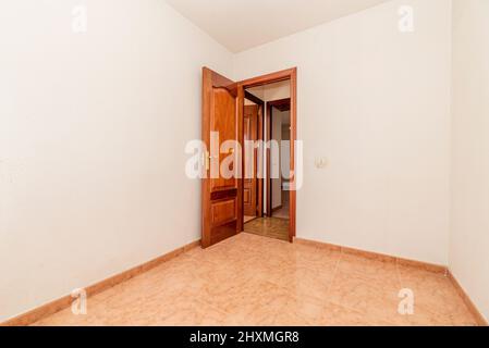 camera vuota con pavimento in gres arancio, porta in legno di mogano e pareti dipinte di bianco Foto Stock