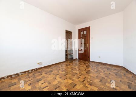 camera vuota con pavimento in legno tipo sintasol, pareti dipinte di bianco, porta in legno e vetro smussato e accesso ad un'altra stanza Foto Stock