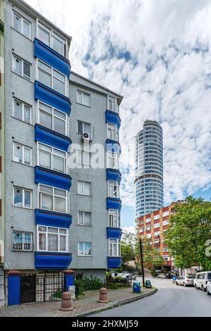 Facciate di edifici residenziali su una strada con giardini e alberi in una giornata di sole con nuvole con una torre ufficio dietro nel quartiere Sisli o Foto Stock