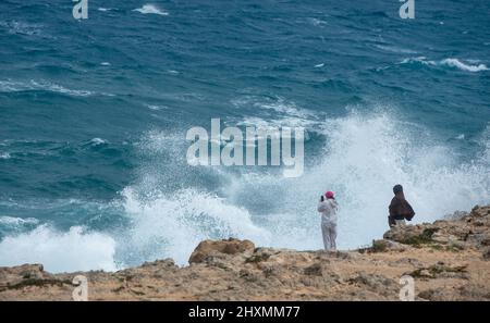 Persone su una costa rocciosa all'oceano tempestoso. Pericolose onde ventose che si infrangono sulle rocce Foto Stock